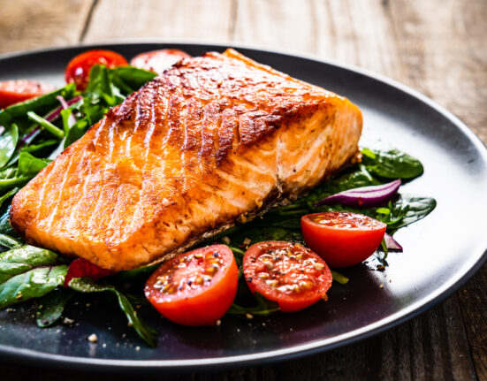 Fried salmon steak with vegetables on wooden table