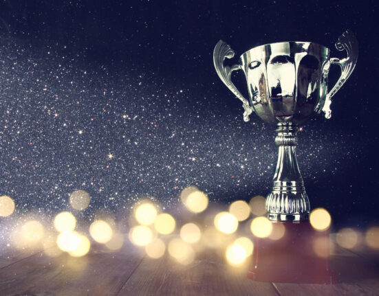 low key image of trophy over wooden table and dark background, with abstract shiny lights