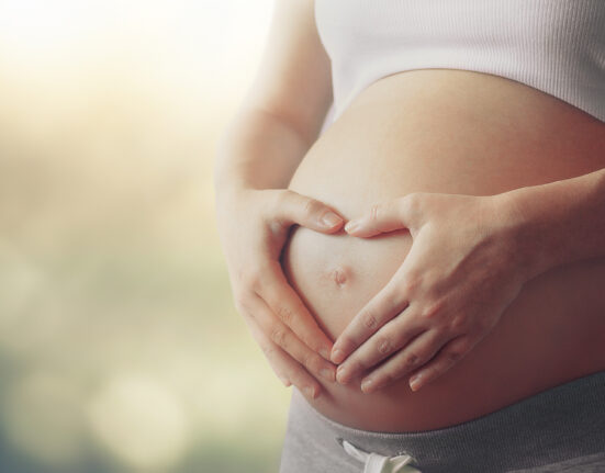 pregnant woman's belly with fingers heart symbol