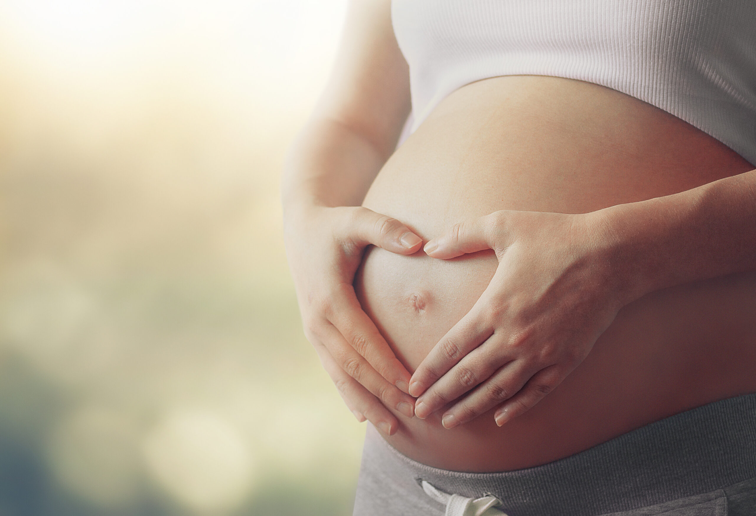 pregnant woman's belly with fingers heart symbol