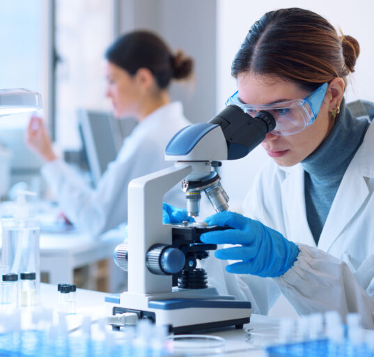 Young scientists conducting research investigations in a medical laboratory, a researcher in the foreground is using a microscope