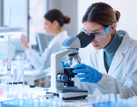 Young scientists conducting research investigations in a medical laboratory, a researcher in the foreground is using a microscope