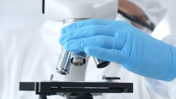 Close up of virologist's hands in blue gloves adjusting microscope in laboratory, conducting scientific research and analysis. Health care, medicine and science concept.
