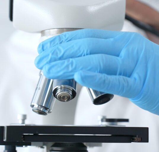 Close up of virologist's hands in blue gloves adjusting microscope in laboratory, conducting scientific research and analysis. Health care, medicine and science concept.
