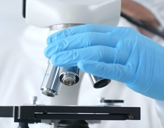 Close up of virologist's hands in blue gloves adjusting microscope in laboratory, conducting scientific research and analysis. Health care, medicine and science concept.