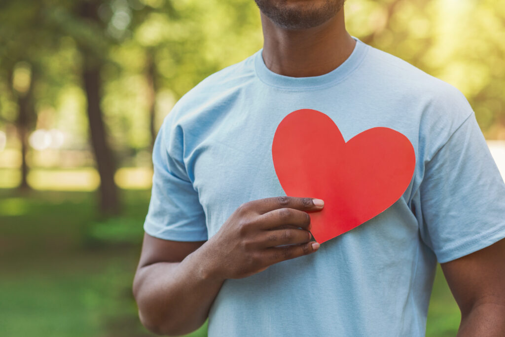 World heart day, volunteering and charity. Millennial african-american man holding red heart on his chest, free space
