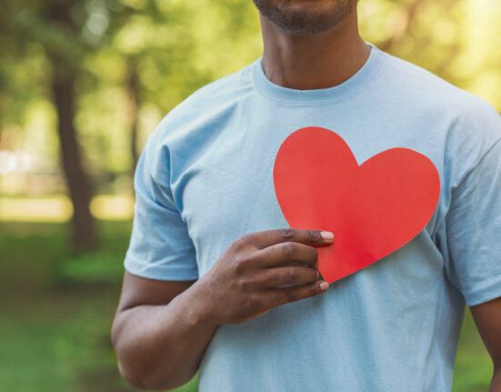World heart day, volunteering and charity. Millennial african-american man holding red heart on his chest, free space