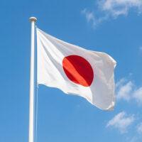 Japanese national flag waving on tall pole against bright blue s