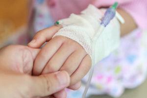 Mother holding child hand with saline IV solution in hospital