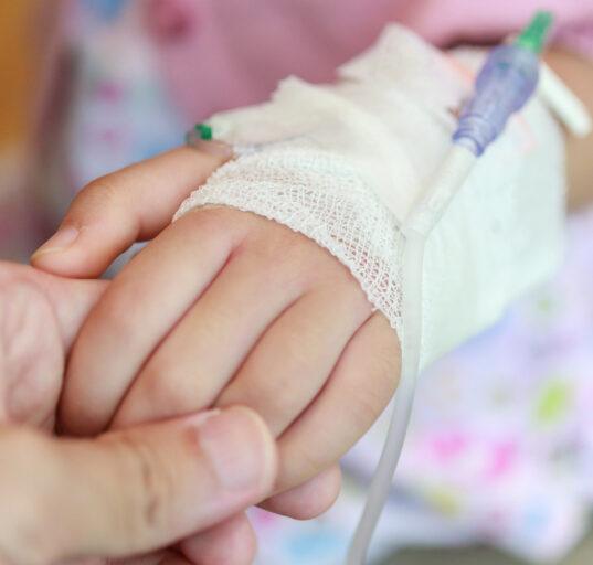 Mother holding child hand with saline IV solution in hospital