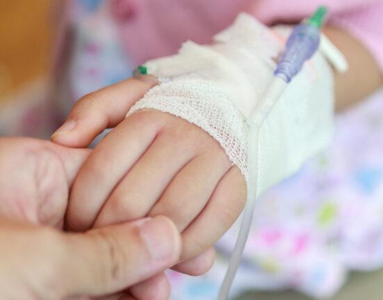 Mother holding child hand with saline IV solution in hospital